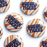 Several round button badges with the Auburn Tigers logo, featuring orange and white tiger stripes and navy blue lettering, arranged on a white background.