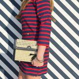 Person wearing a red and blue striped dress holding a gold clutch against a striped background