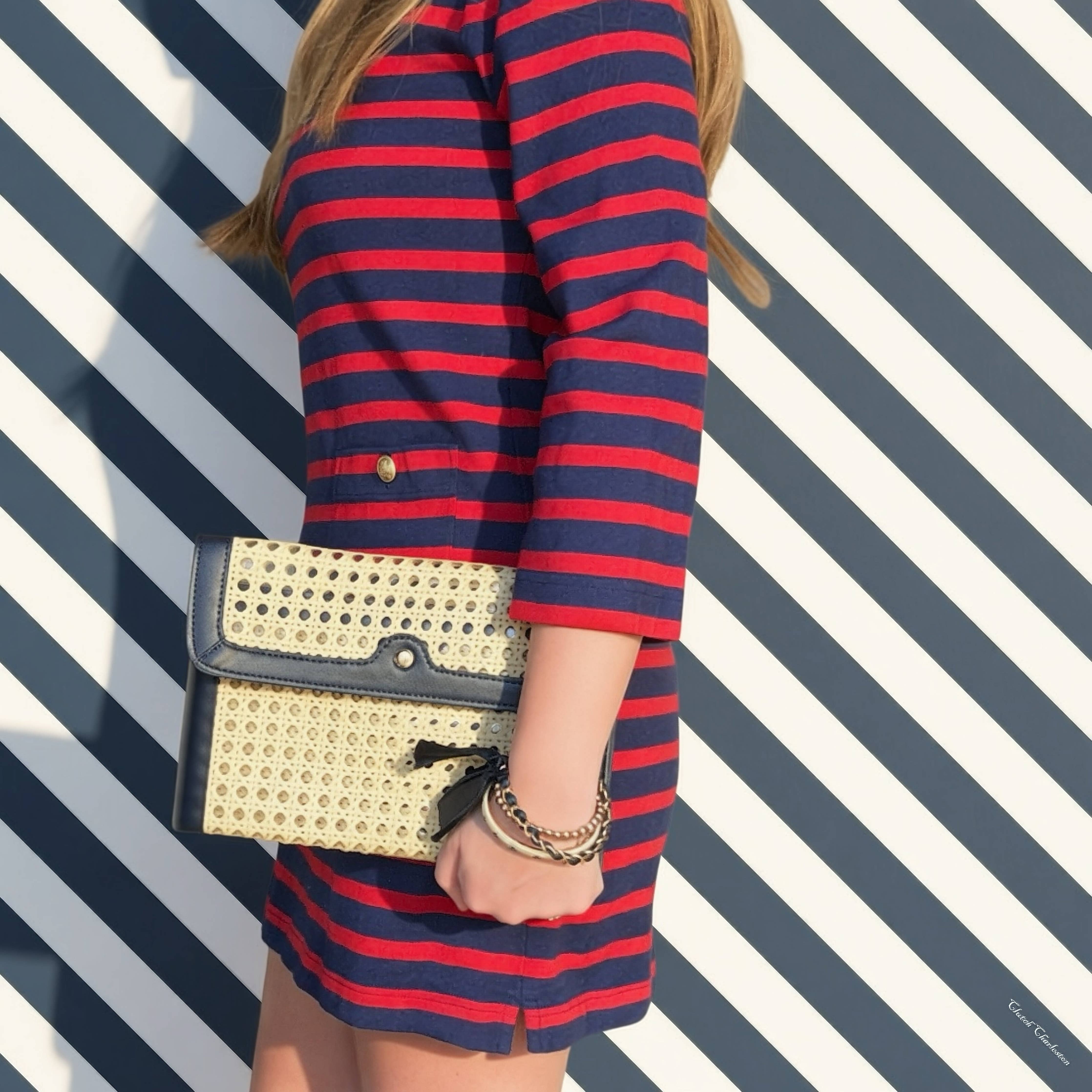 Person wearing a red and blue striped dress holding a gold clutch against a striped background