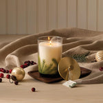 Candle with a nature-themed design on a wooden tray with decorative items.