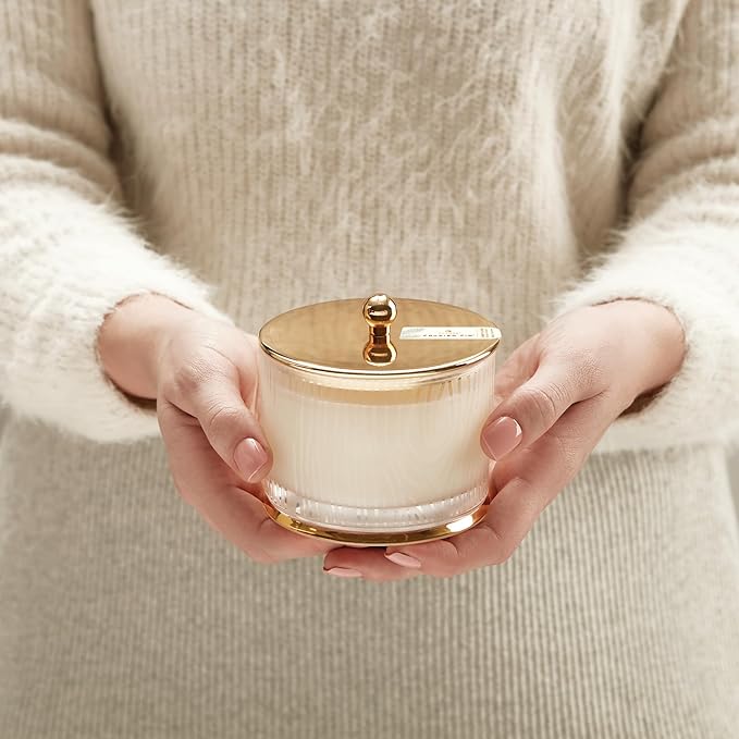 Person holding a white container with a gold lid against a neutral background