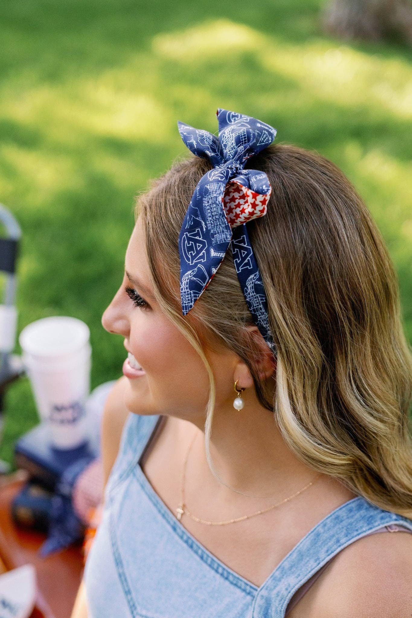 A woman outdoors wearing a blue patterned fabric headband with a red and white polka dot accent, paired with a light blue denim top.