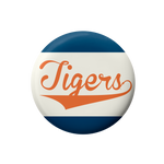 A round button badge featuring the word 'Tigers' in orange script across a white center, with dark blue bands at the top and bottom, shown on a plain white background.