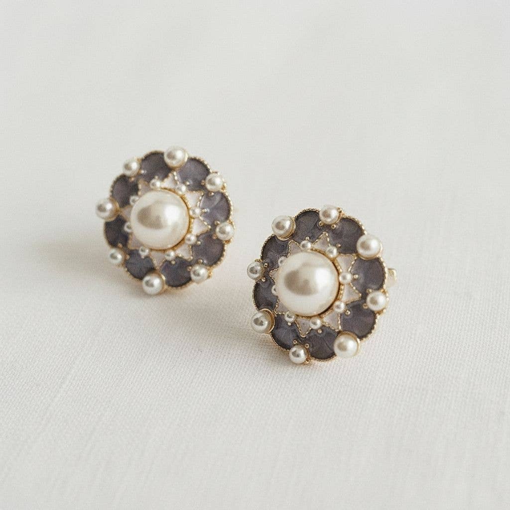 Pair of earrings with pearl center and dark gemstone accents on a light background