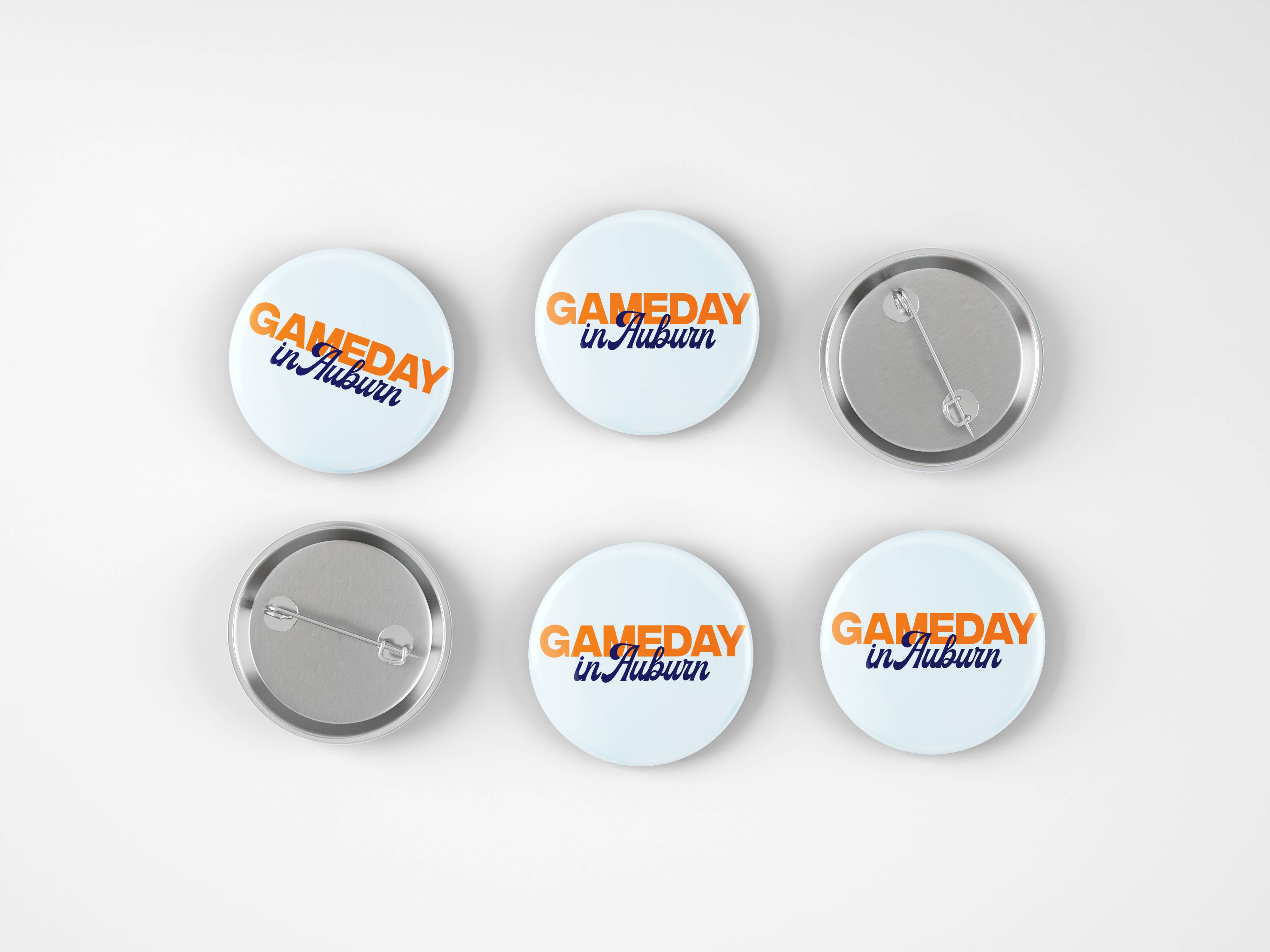 Six round pin-back buttons shown on a light gray background, including three front views and three back views. The front buttons have a white background with orange and blue text reading 'GAMEDAY in Auburn'.