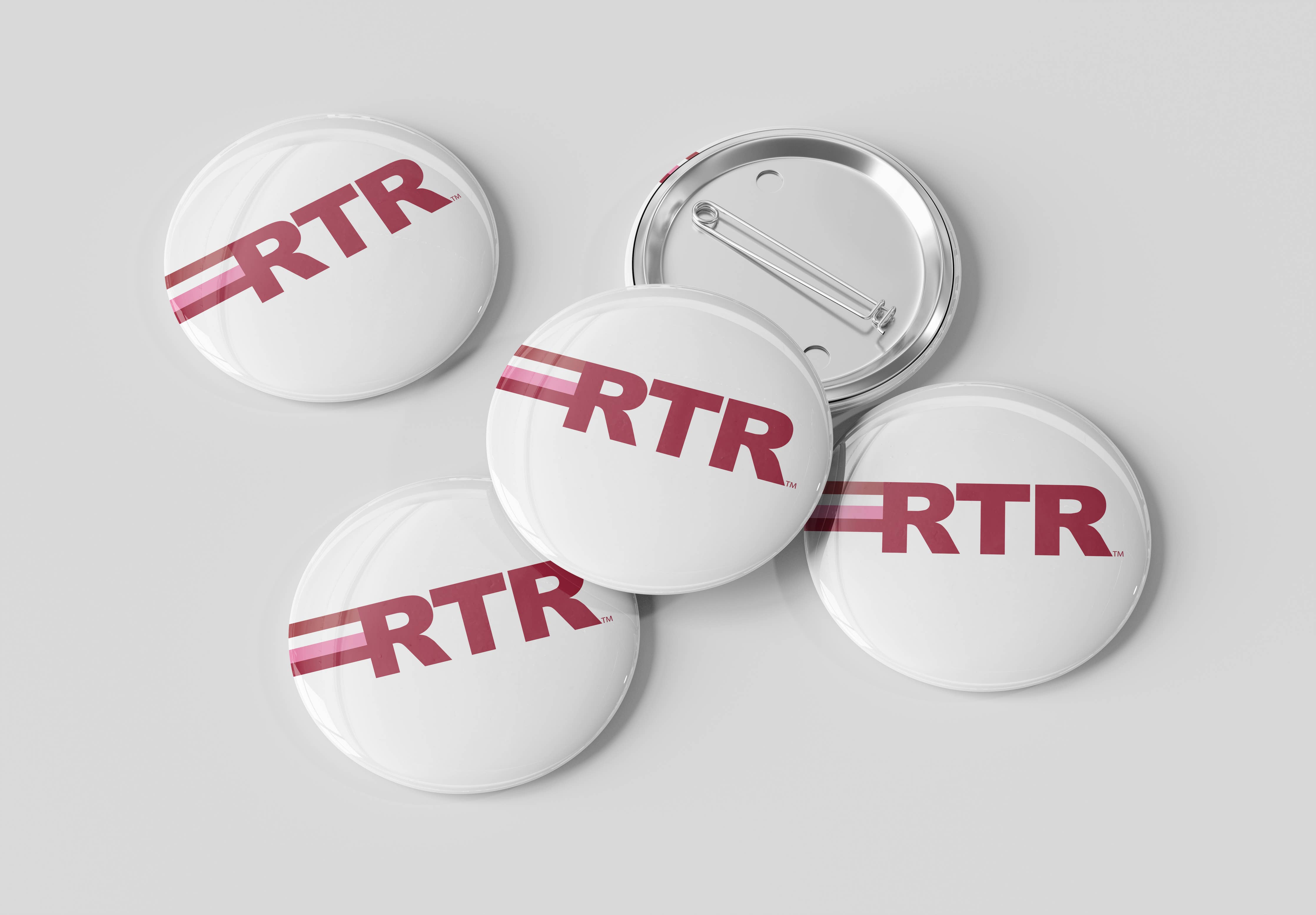 Five round pin-back buttons with a glossy white surface, featuring the red letters 'RTR' with two thin red stripes, shown on a light gray background. One button is turned over to show the silver metal pin-back mechanism.