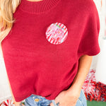 Red sweater with a colorful circular patch worn by a person, with a blurred background.