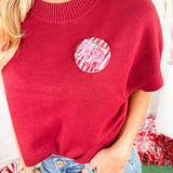 Red sweater with a colorful circular patch worn by a person, with a blurred background.