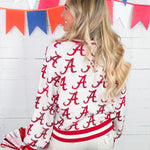 Woman wearing a white jacket with red 'A' pattern, holding pom-poms, in front of colorful flags.