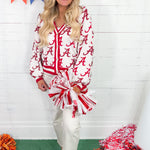Woman wearing a red and white patterned shirt with pom-poms in front of a white wall with colorful flags.