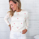 Woman wearing a white sweater with red heart patterns against a white wooden background