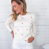 Woman wearing a white sweater with red heart patterns against a white wooden background