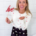Woman holding a 'love' sign with hearts against a white brick wall