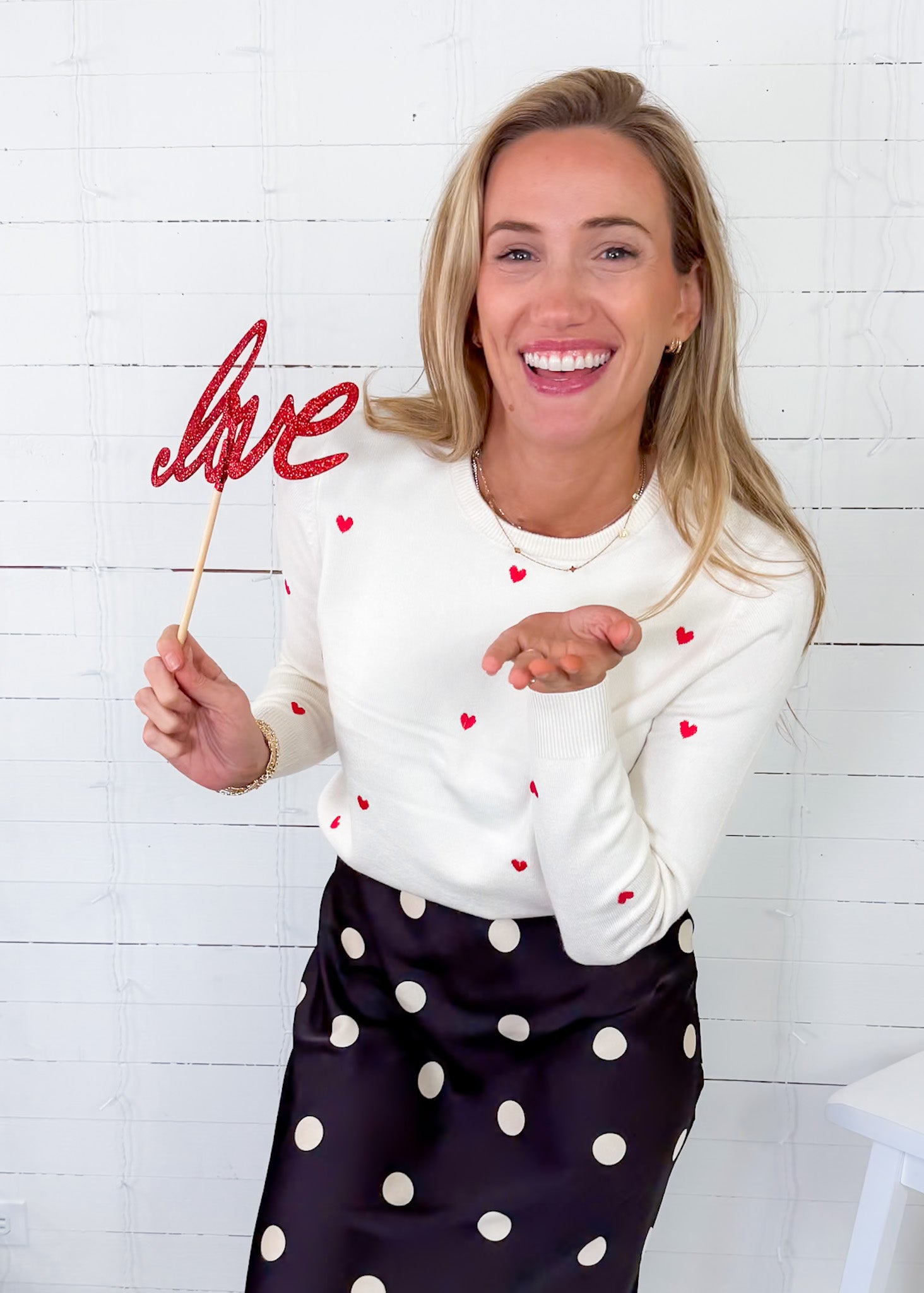 Woman holding a 'love' sign with hearts against a white brick wall