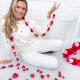Woman sitting on a white floor with heart-shaped decorations and a pink and red pom-pom garland.