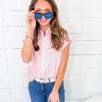 Woman wearing a red and white checkered shirt, blue jeans, and sunglasses against a white wooden background