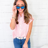 Woman wearing a red and white checkered shirt, blue jeans, and sunglasses against a white wooden background