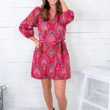 Woman wearing a pink patterned dress with beige boots against a white wooden background