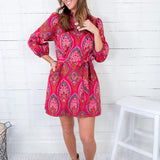 Woman wearing a pink patterned dress with beige boots in a room with white wooden walls.