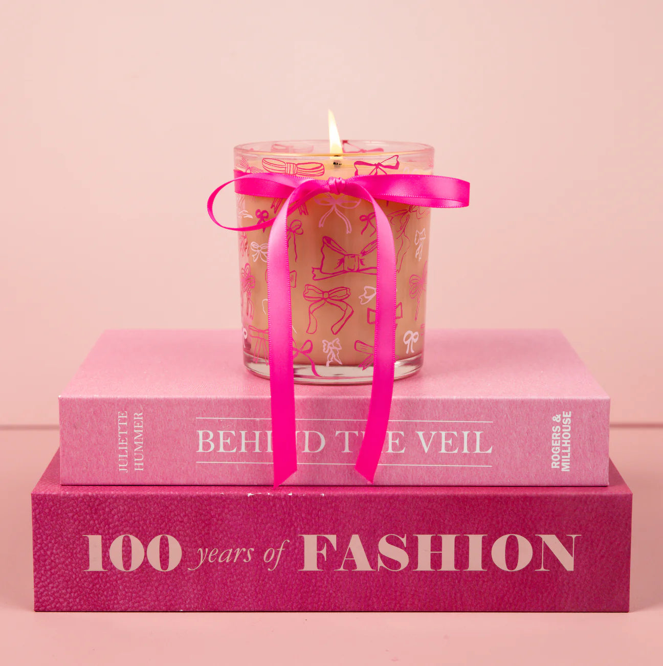 Candle with a pink ribbon on top of two pink books against a light pink background