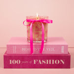 Candle with a pink ribbon on top of two pink books against a light pink background