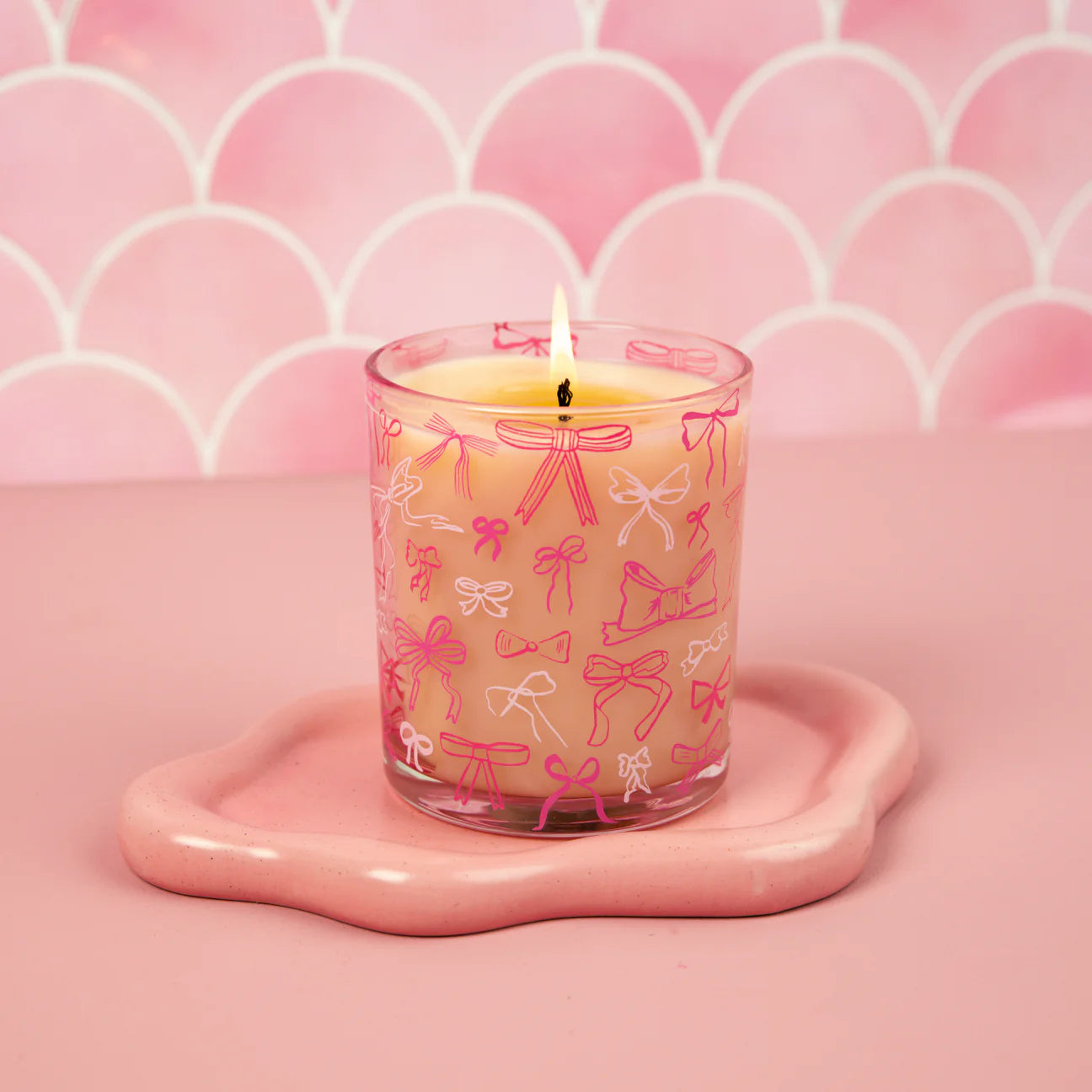 Candle in a glass holder with pink bow design on a pink background