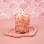 Candle in a glass holder with pink bow design on a pink background