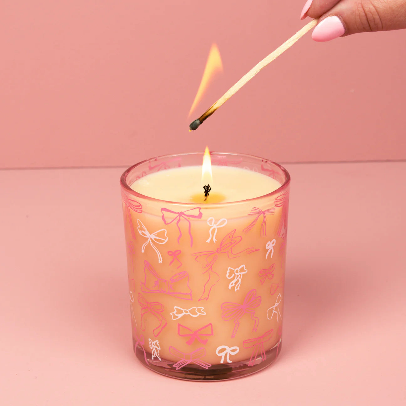 Candle with bow pattern being lit with a match against a pink background