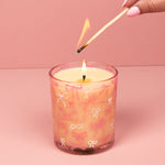 Candle with bow pattern being lit with a match against a pink background