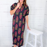 Woman wearing a floral dress standing next to a white stool against a white wooden panel background