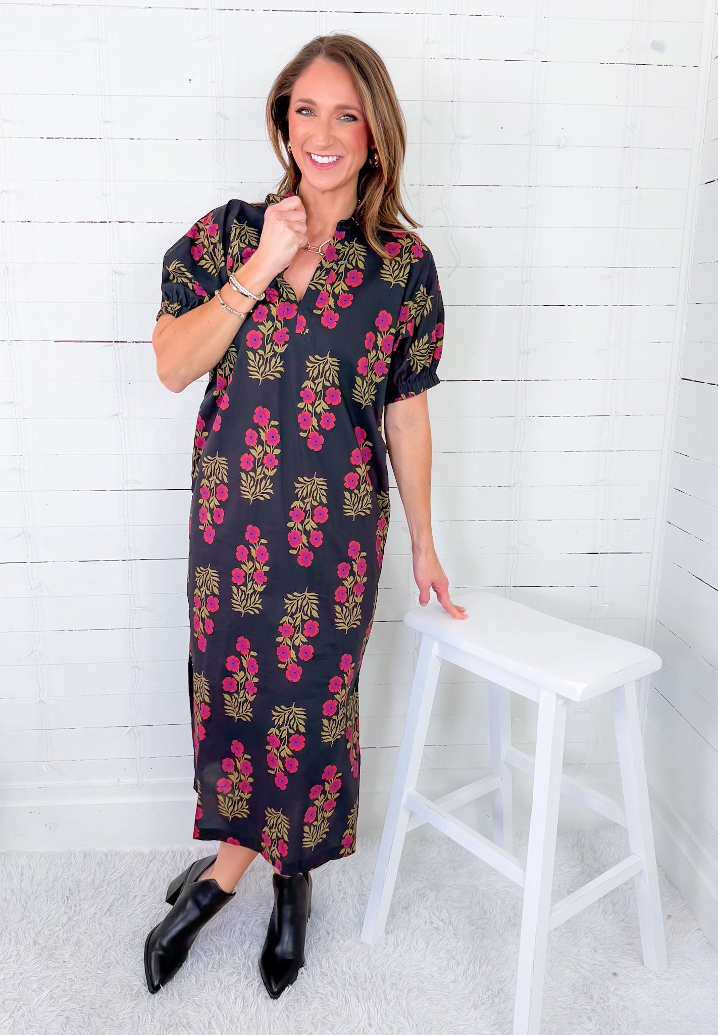 Woman wearing a floral dress standing next to a white stool against a white wooden panel background