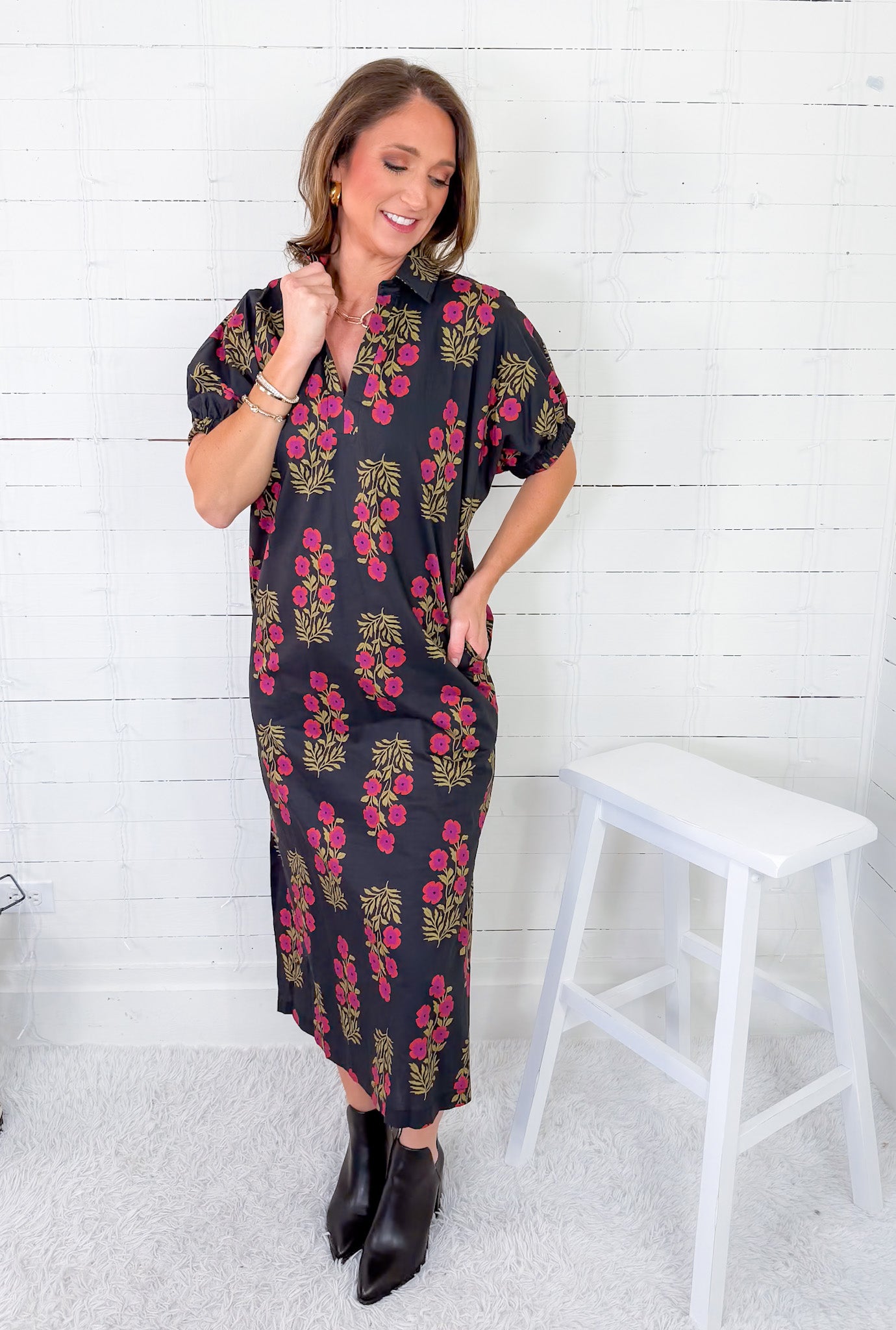 Woman wearing a floral dress standing next to a white stool against a white wooden panel background