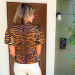 Woman wearing a tiger print top standing in front of a door.