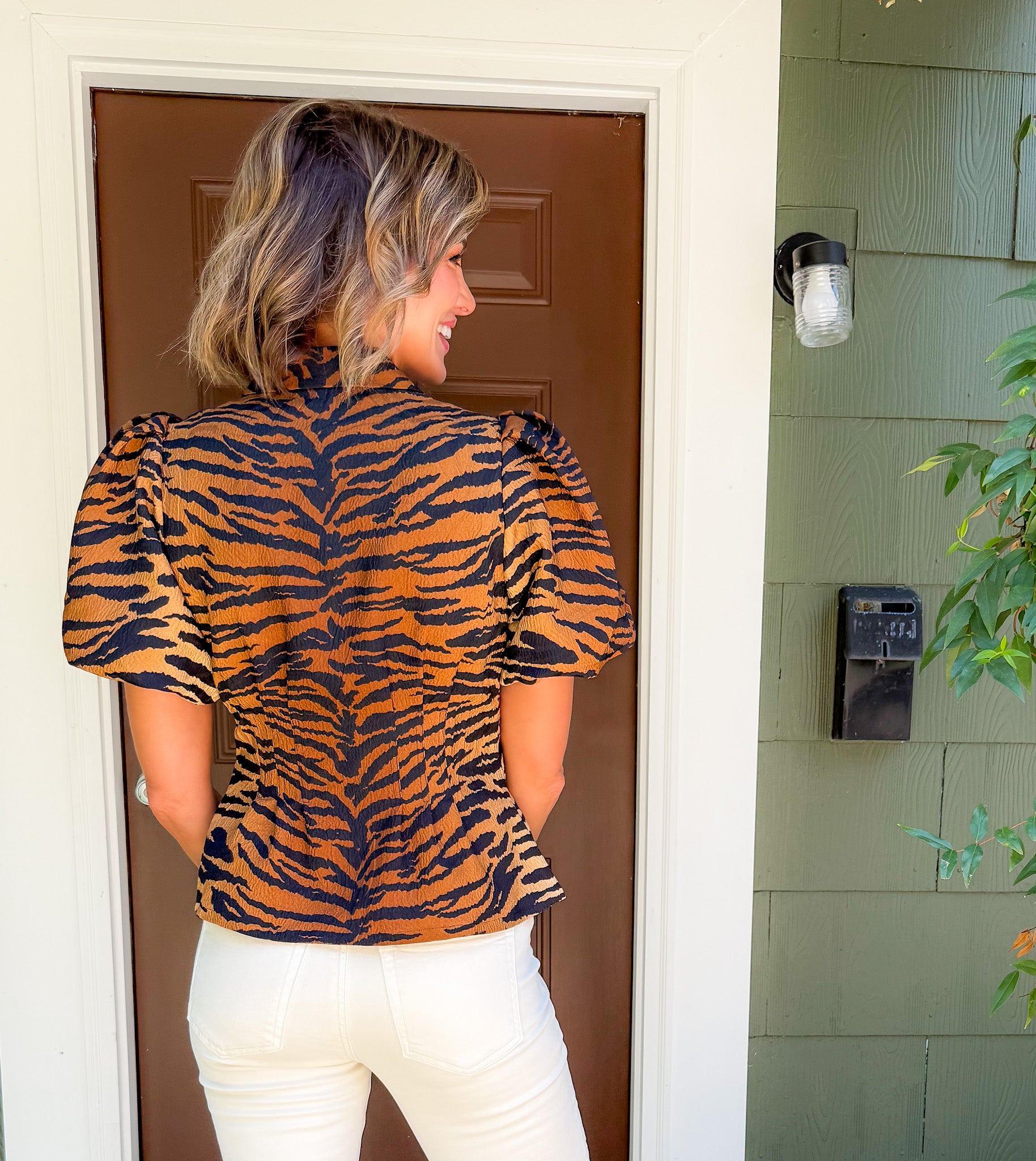 Woman wearing a tiger print top standing in front of a door.
