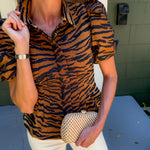 Woman wearing a tiger print shirt and holding a clutch in front of a building.