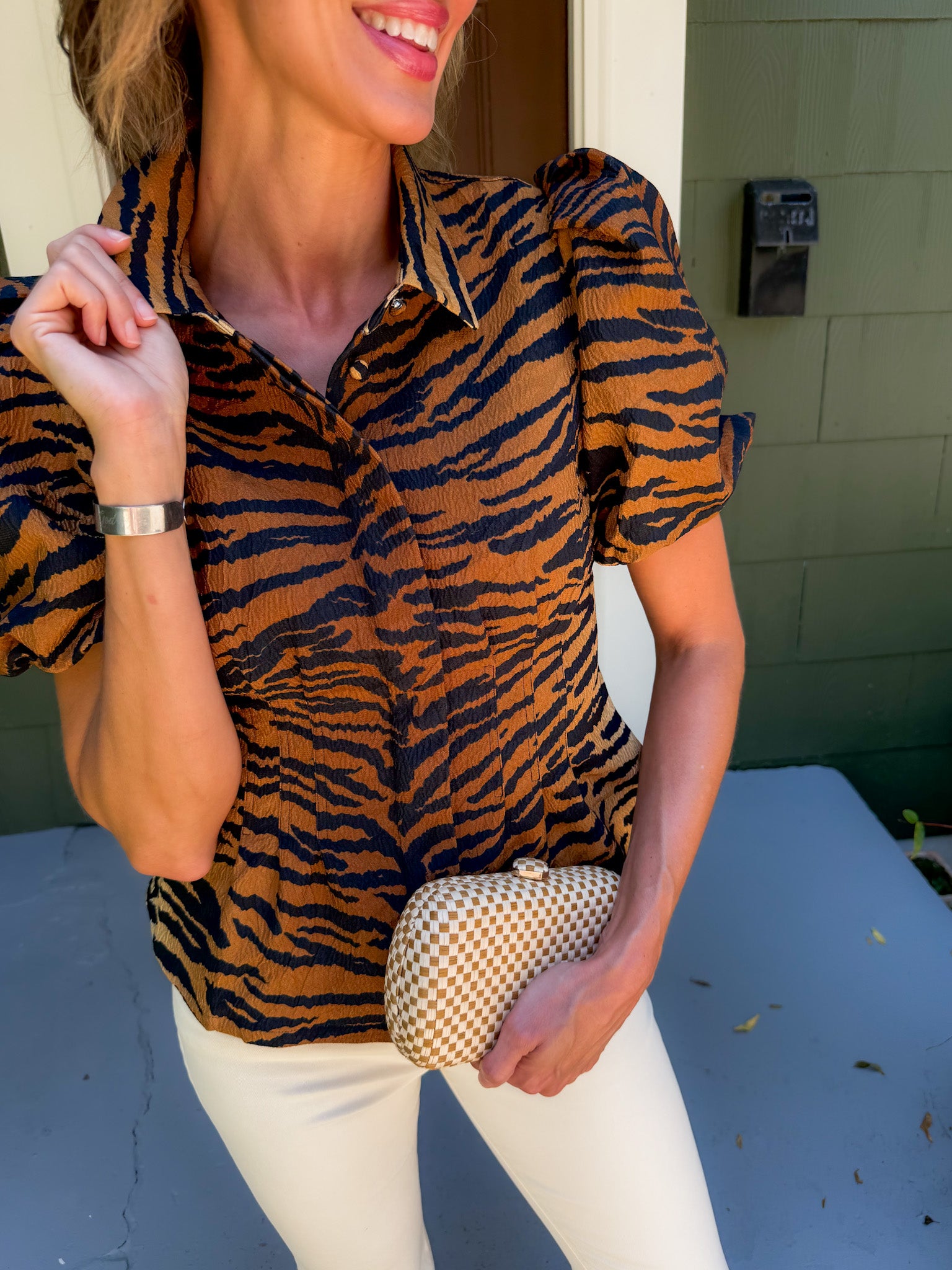 Woman wearing a tiger print shirt and holding a clutch in front of a building.
