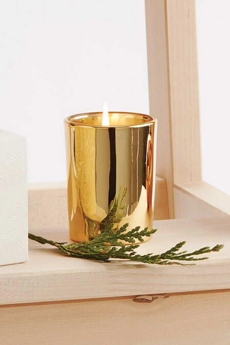 Gold candle holder with a lit candle and greenery on a wooden surface.
