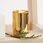 Gold candle holder with a lit candle and greenery on a wooden surface.