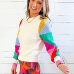 Woman wearing a colorful sweater and patterned skirt against a white wooden background