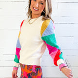 Woman wearing a colorful sweater and patterned skirt against a white wooden background