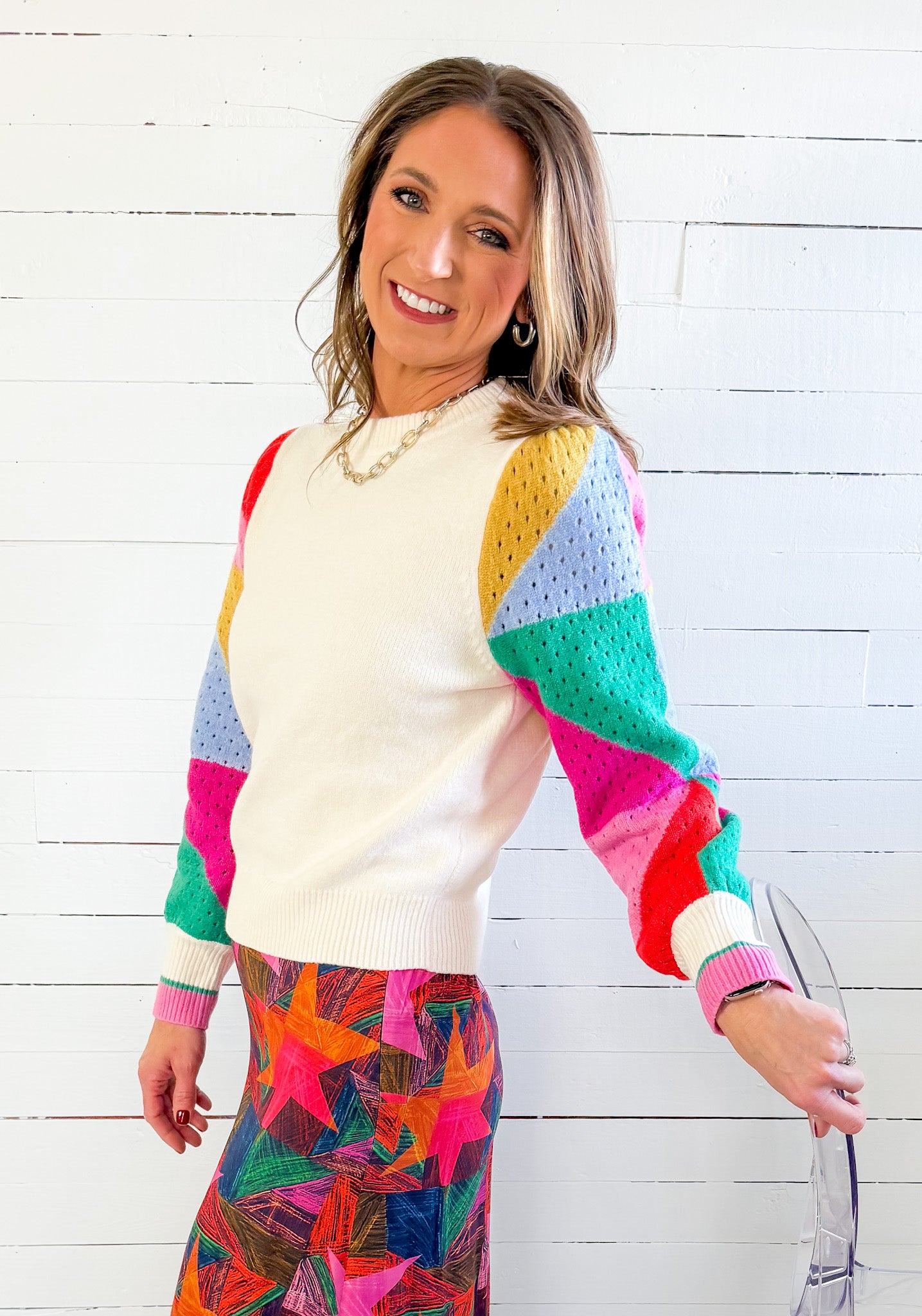 Woman wearing a colorful sweater and patterned skirt against a white wooden background