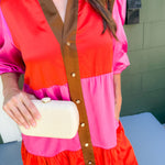 Person wearing a colorful dress with a vest, holding a clutch.