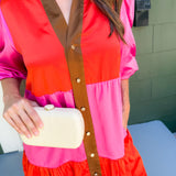 Person wearing a colorful dress with a vest, holding a clutch.