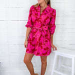 Woman wearing a bright pink floral dress against a white wooden background