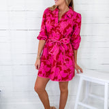 Woman wearing a bright pink floral dress against a white wooden background
