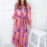 Woman wearing a colorful dress with a belt, standing against a white wooden panel background.