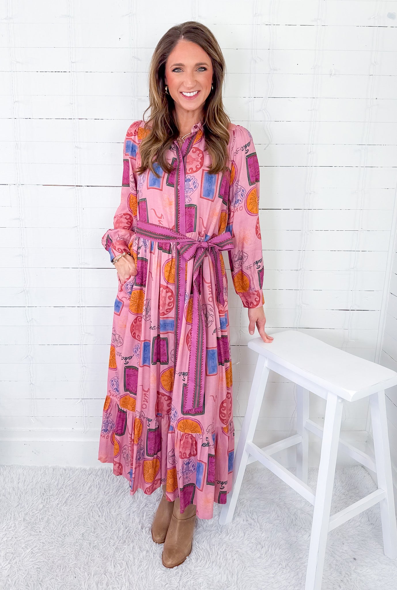 Woman wearing a colorful dress with a belt, standing against a white wooden panel background.