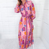 Woman wearing a colorful dress with geometric pattern against a white wooden panel background