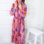 Woman wearing a colorful patterned dress standing against a white wooden panel background
