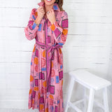 Woman wearing a colorful patterned dress standing against a white wooden panel background